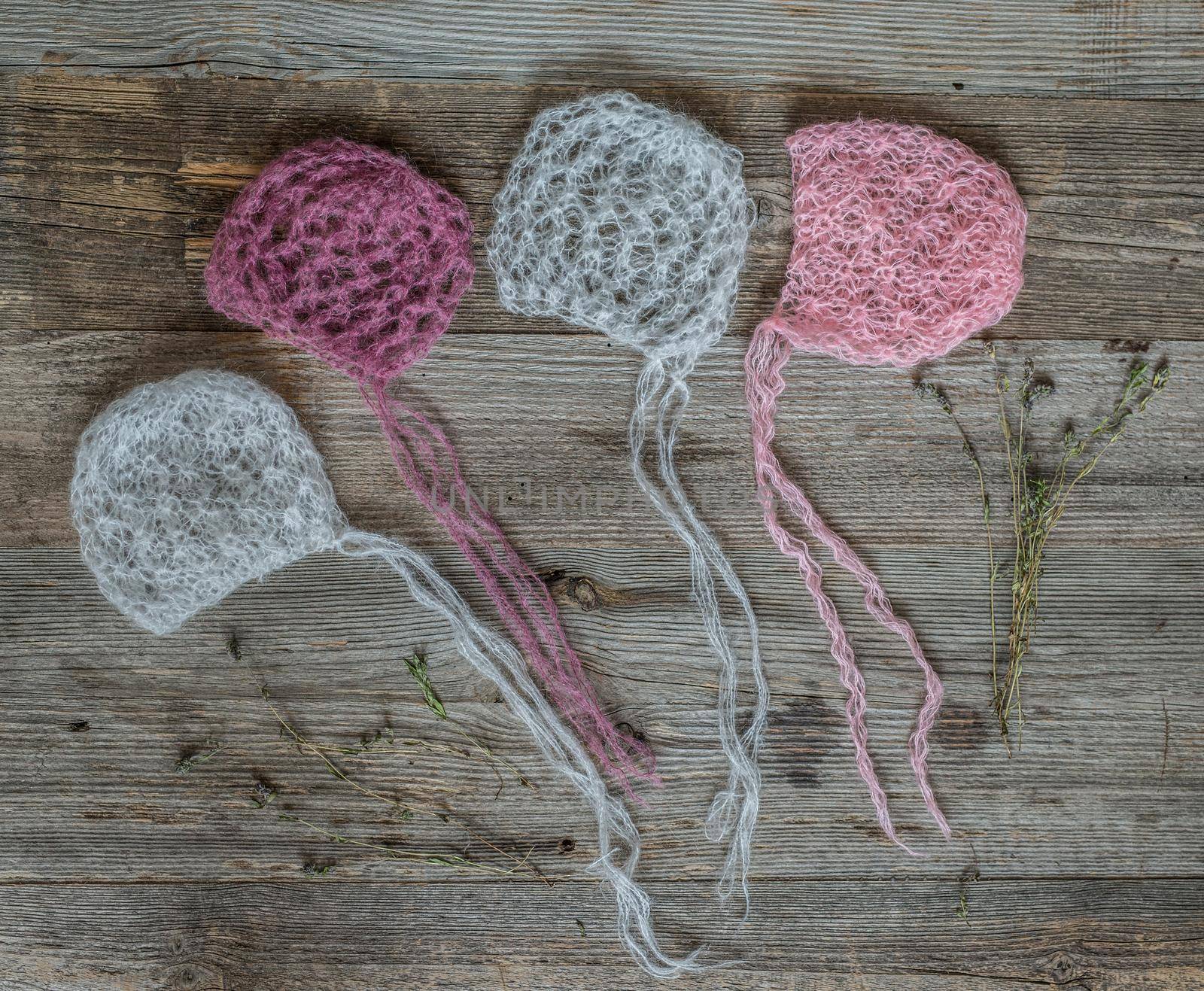 set of tender knitted pink and white hats for newborn on wooden background