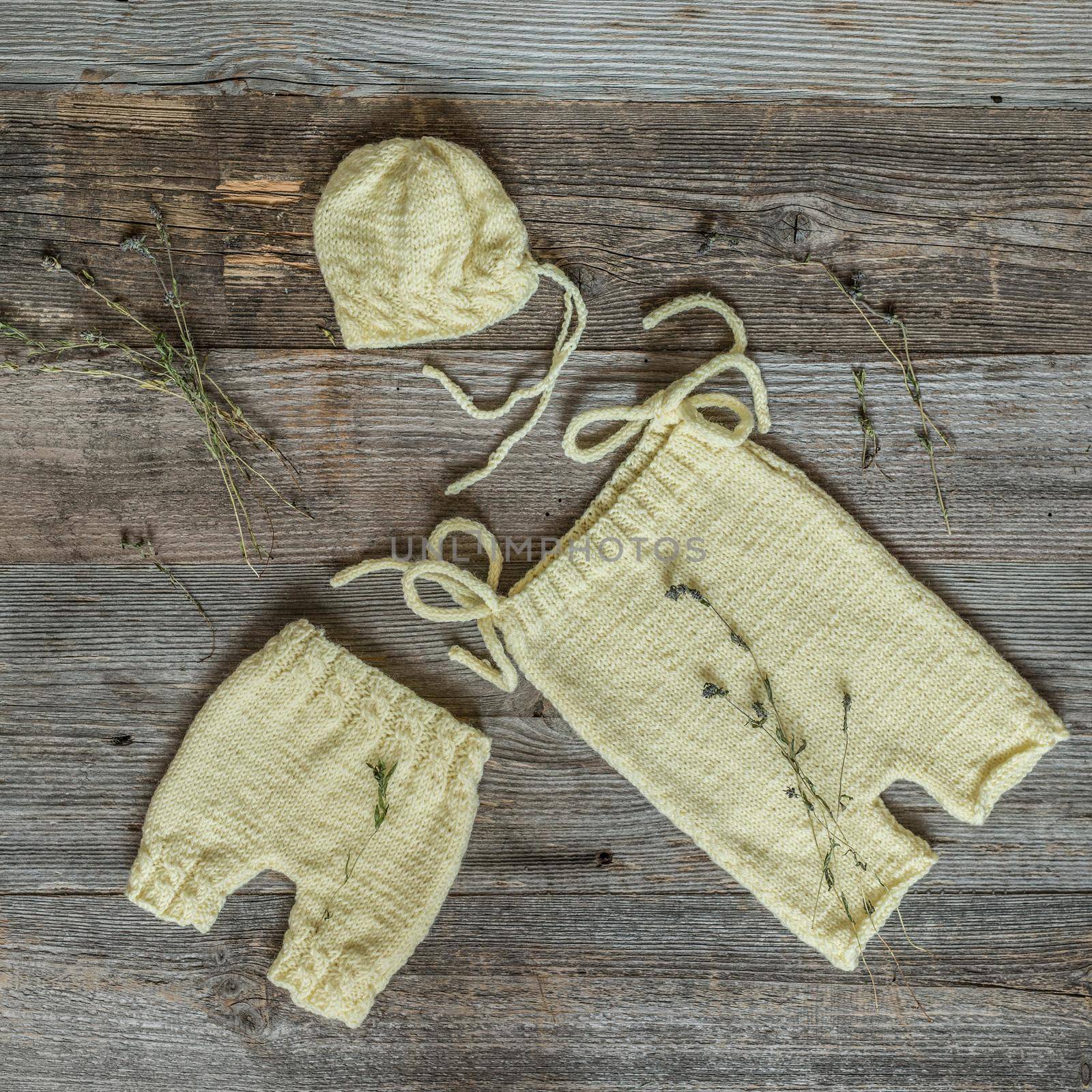 beautiful handmade yellow hat and pants for newborn baby on wooden background, top view