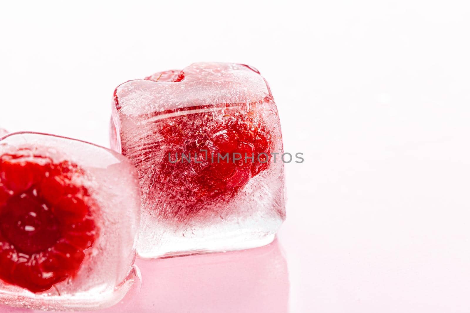 Raspberry ice cubes on pink glossy background. Close up.