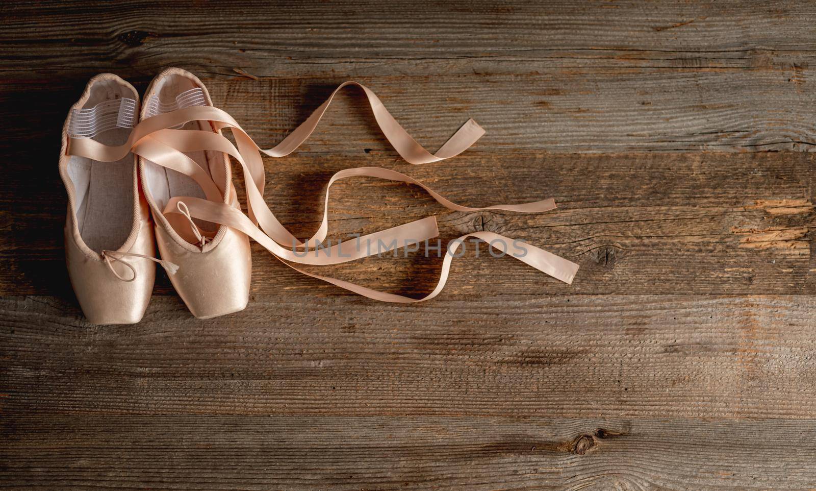 Pink pointe shoes with ribbons on wooden background, top view