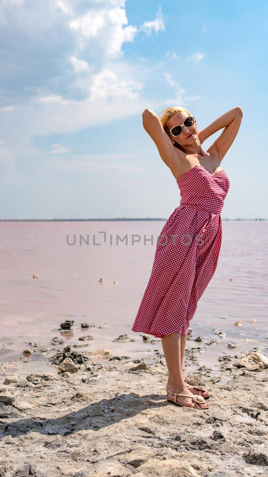 Beautiful girl in a red dress on a red salt lake with blue clouds, glasses of sunglasses