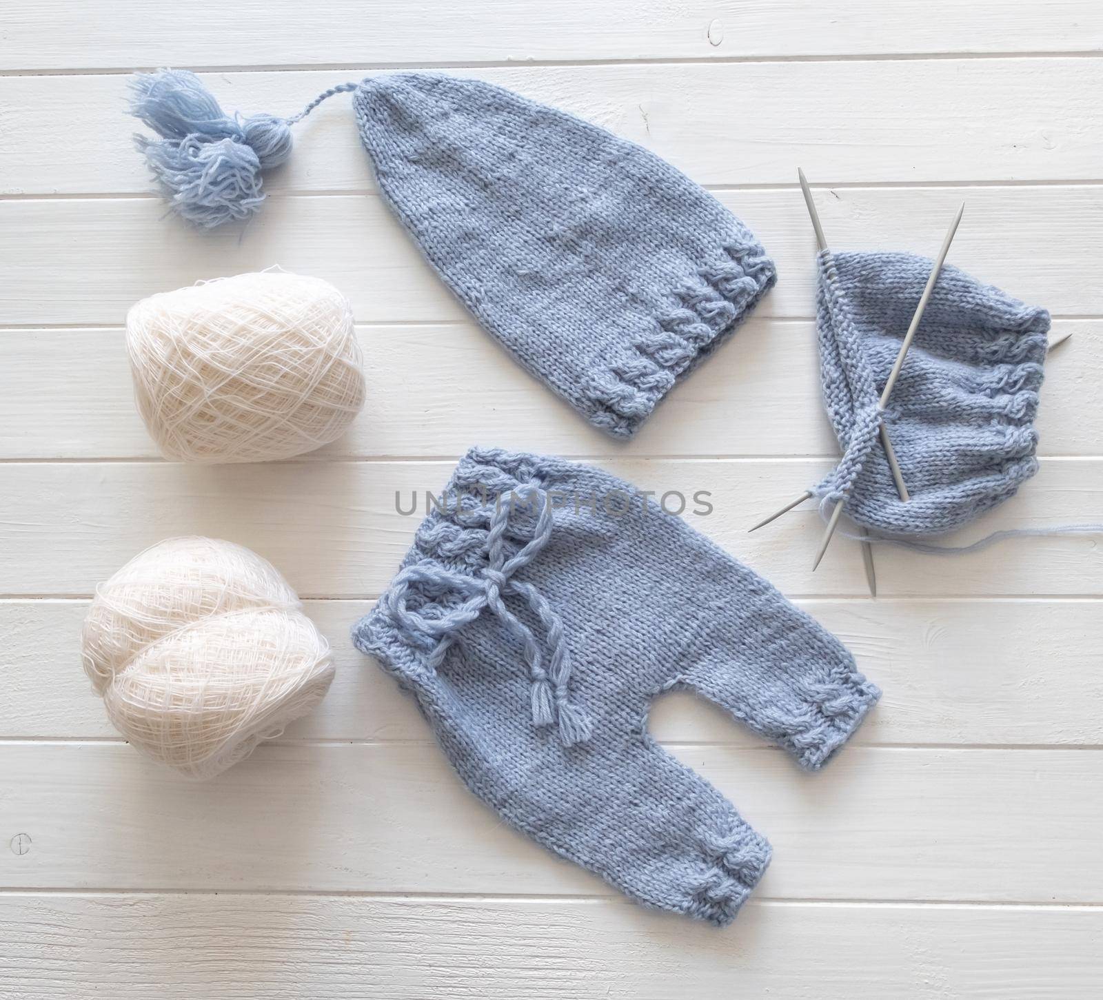 Blue knitted baby clothes with white knitting yarns composed on the white table