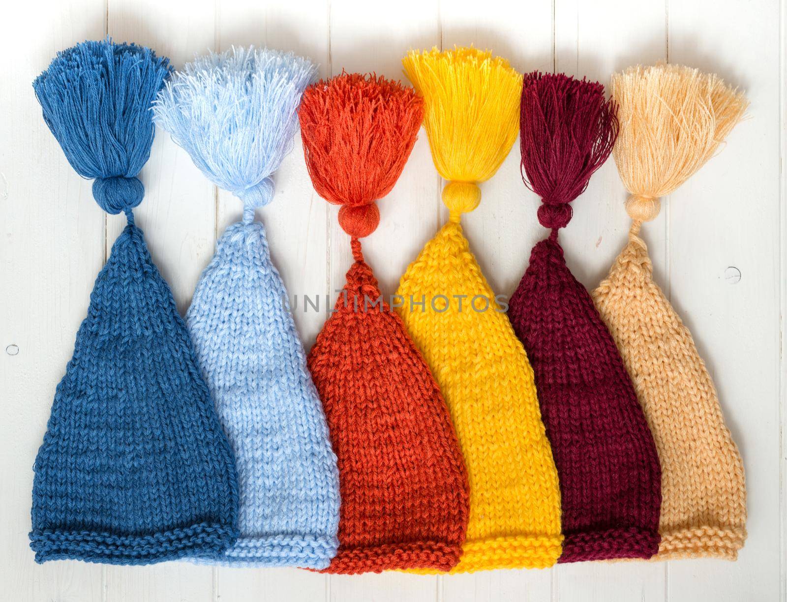 colorful baby knitted hats folded in row on white painted table, top view