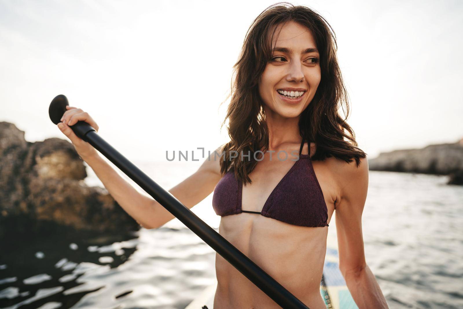 Beautiful young woman sitting on a stand up paddle board in sea on sunset