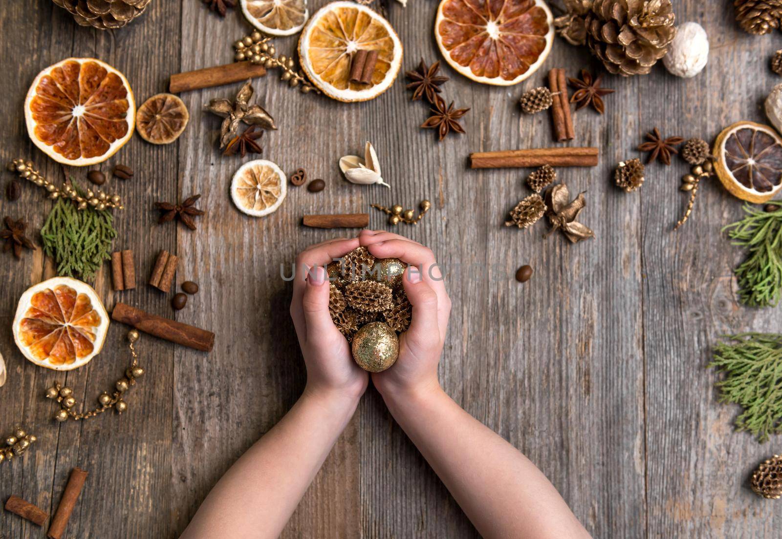 children's hands and Christmas decorations on an old wooden background with cinnamon and dried orange slices