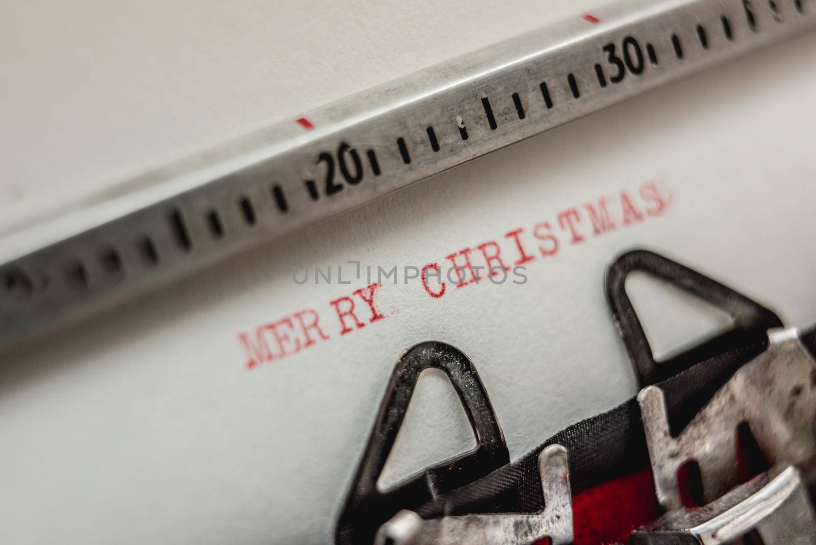 Text Merry Christmas printed with red inks on white paper on retro typewriter. Closeup view