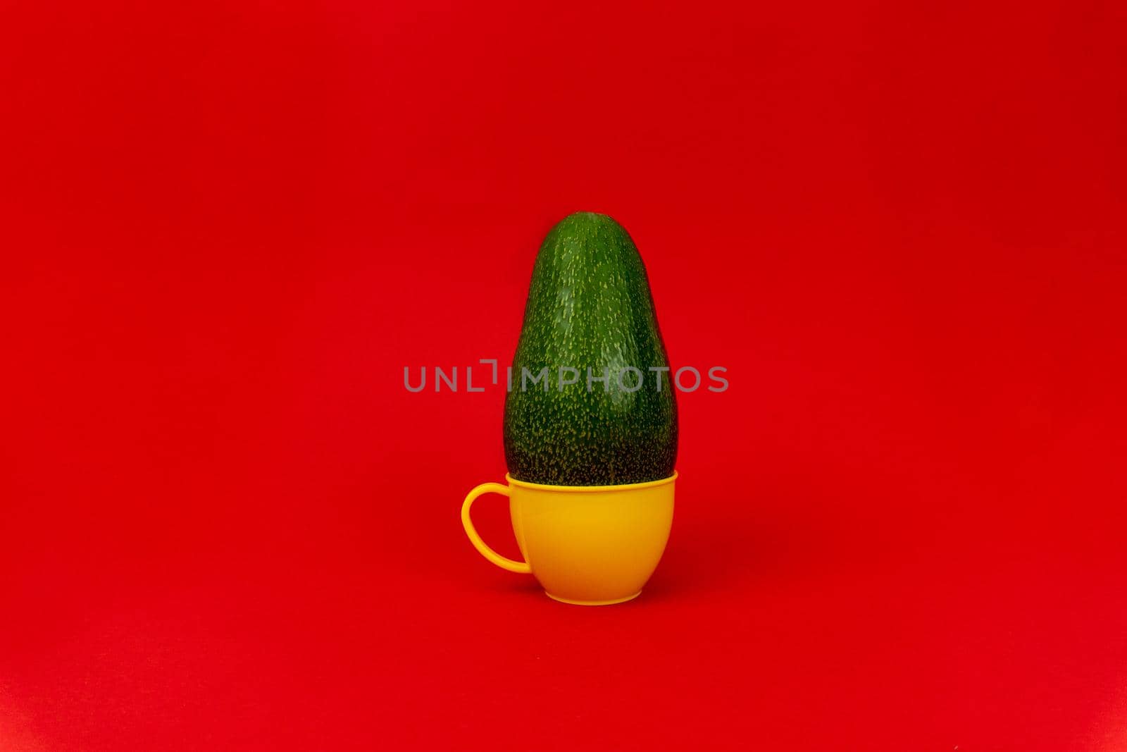 Green avocado in a plastic yellow mug in red background, minimalistic concept, enough space for text.