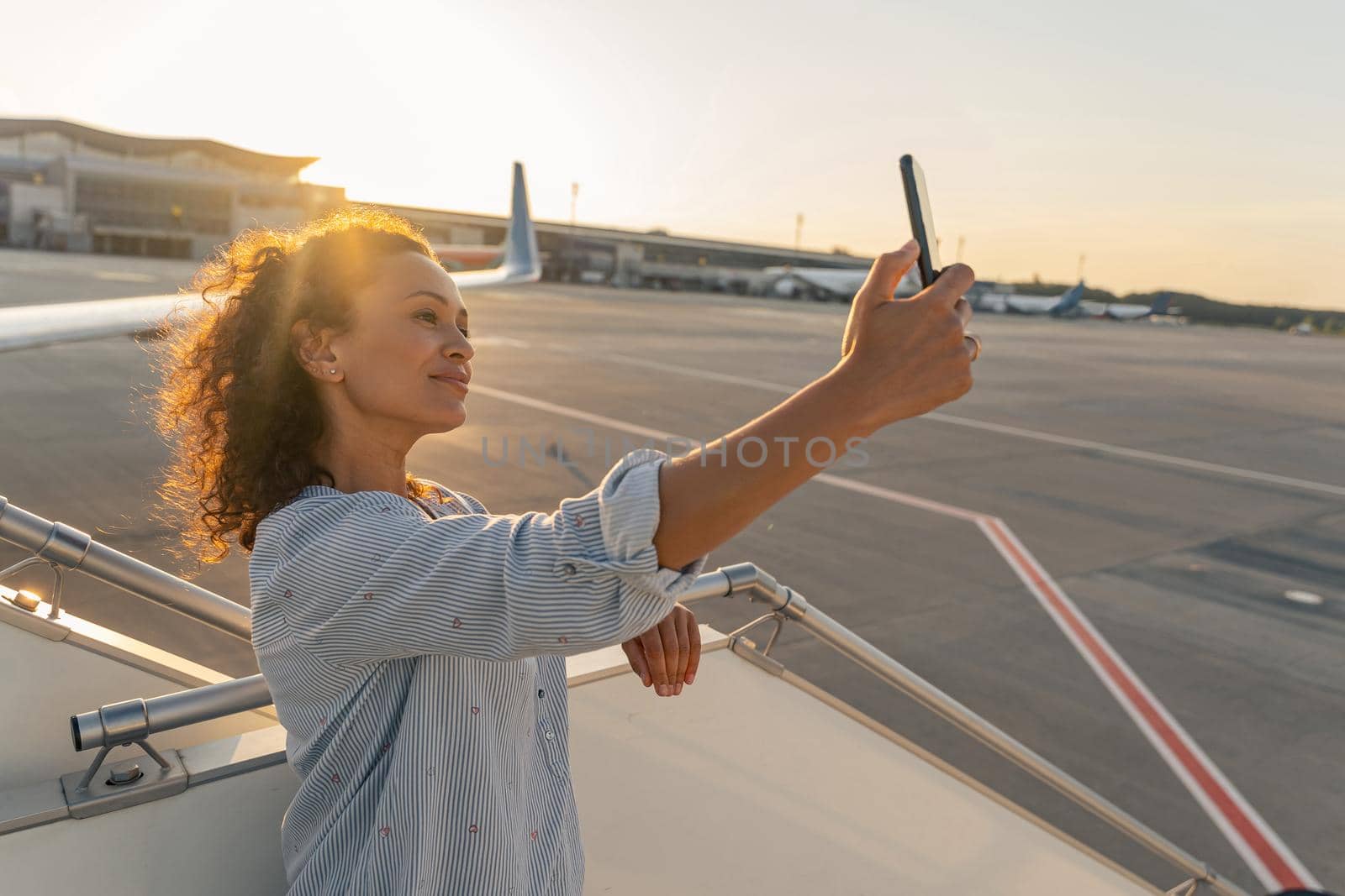 Smiling young woman making selfie on smartphone in airport by Yaroslav_astakhov