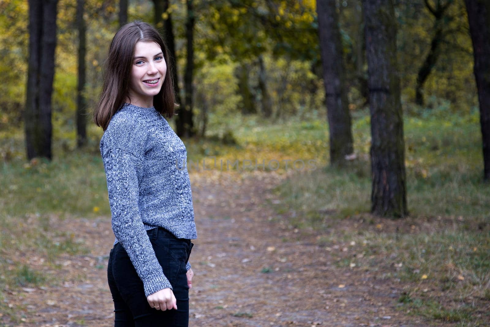 cute girl in a gray sweater is half a turn on the road in the autumn forest. Copy space area.