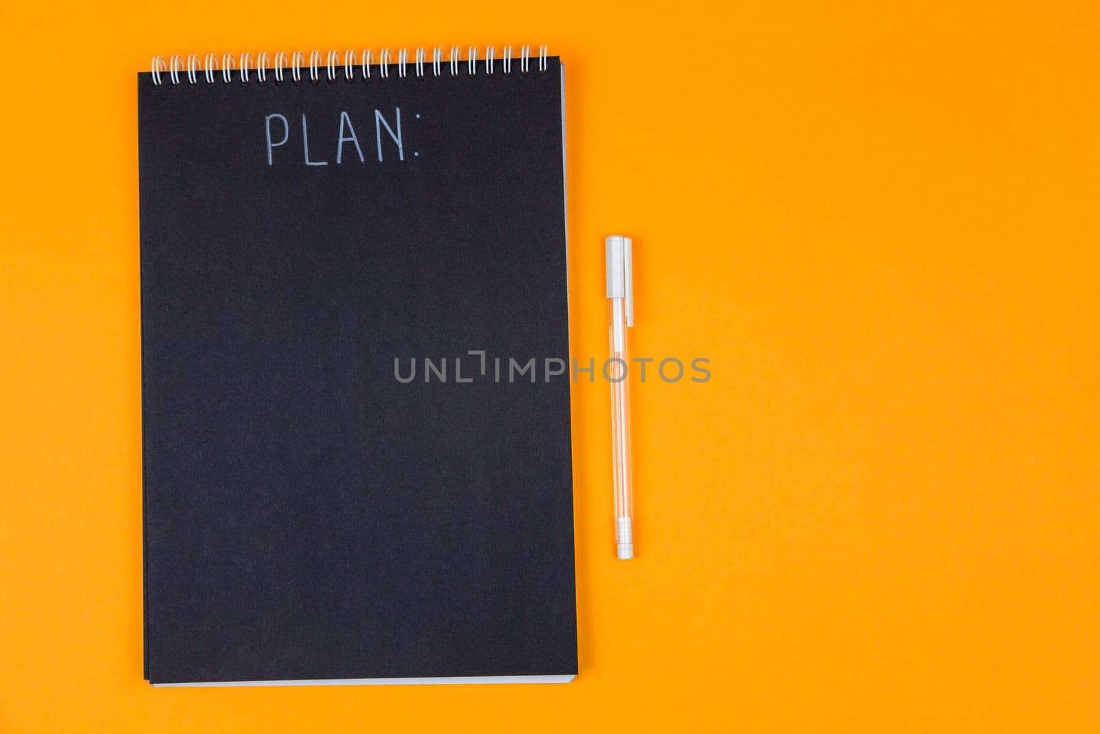 Wide view image of blank black spiral note pad and white marker with calligraphic inscription plan on yellow background