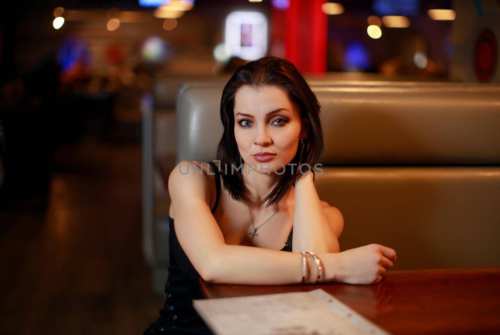 Beautiful young lady alone in bar sitting, menu on table
