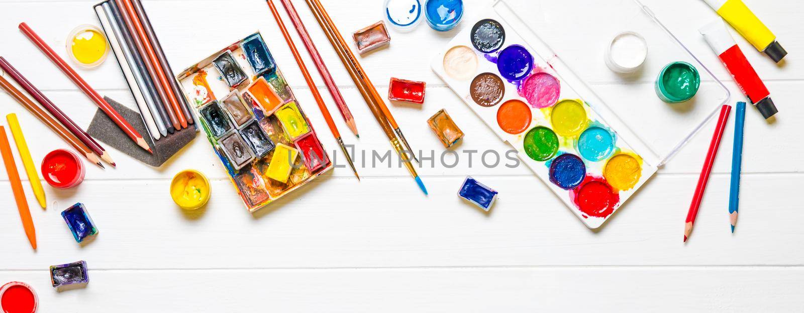 Watercolor paints with brushes and colored pencils on white wooden background, top view. Creative art concept