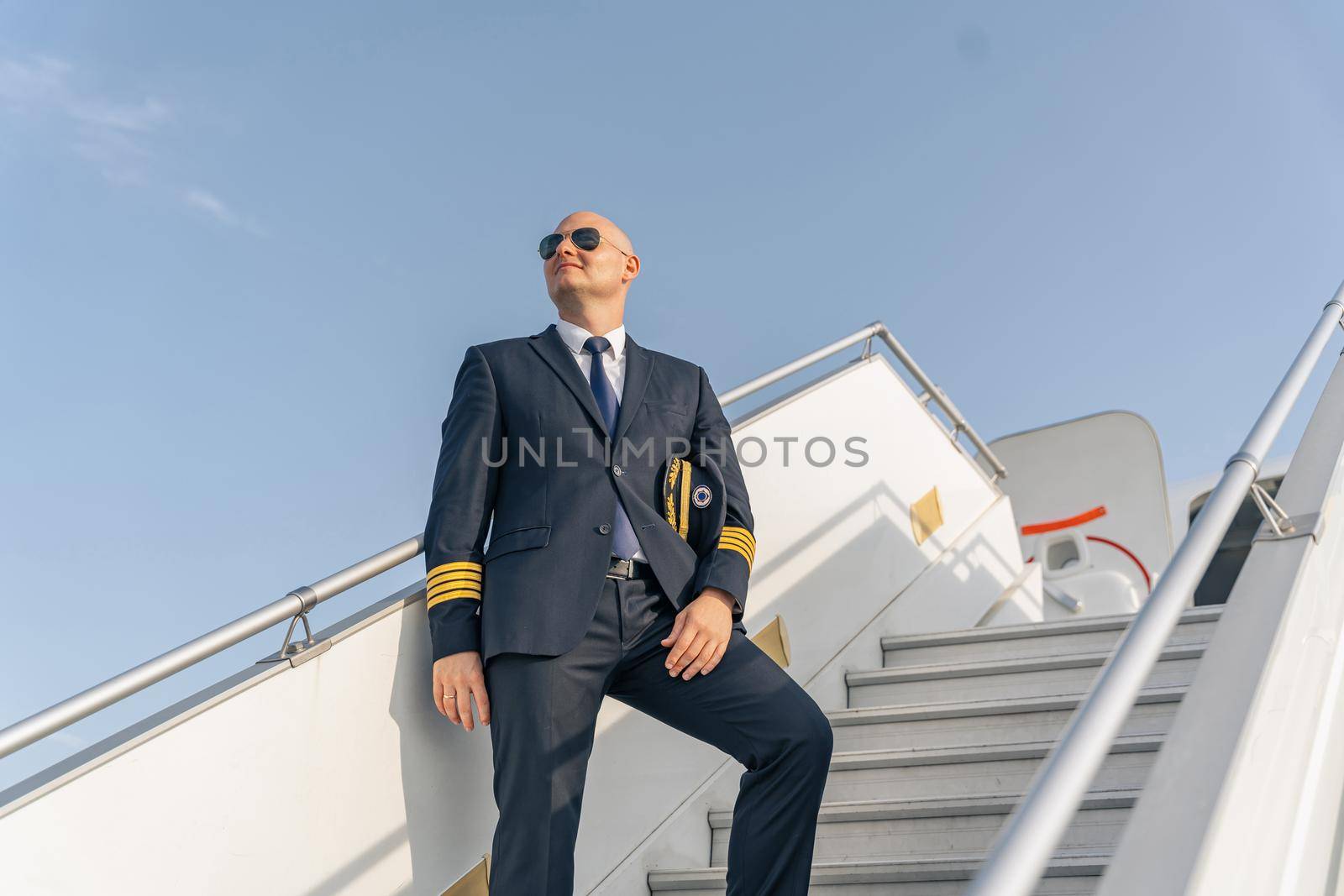 Smiling pilot looking away on plane ladder by Yaroslav_astakhov