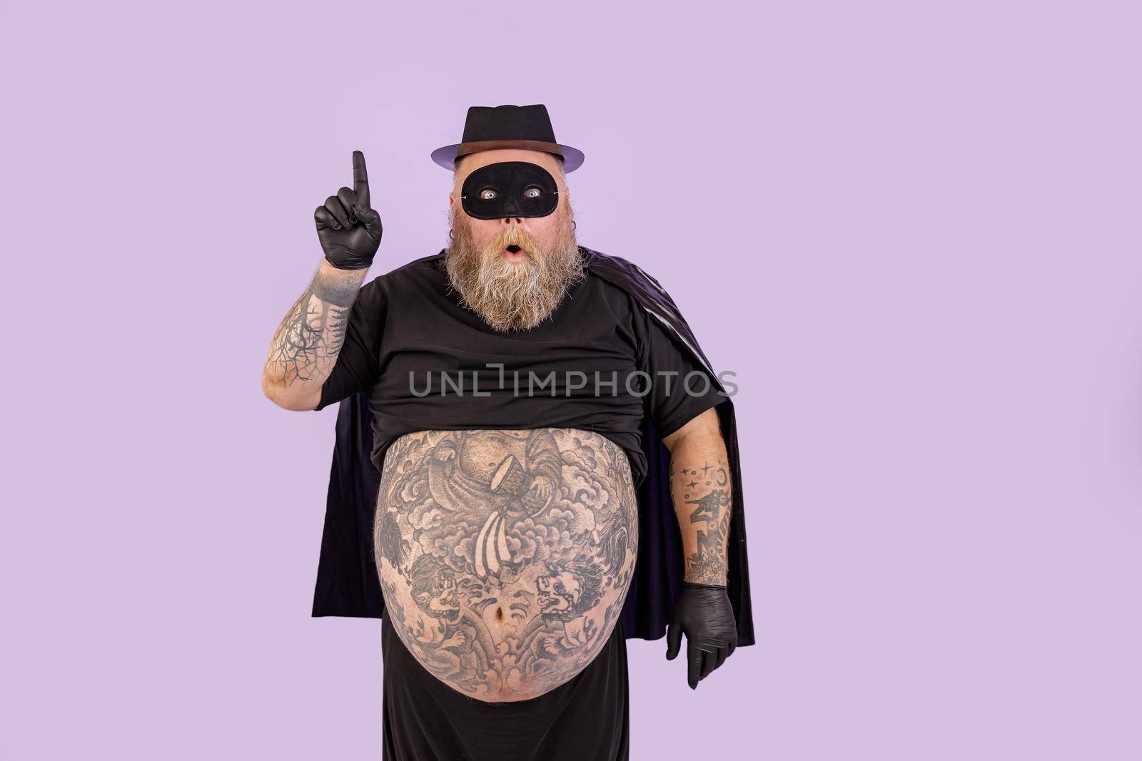 Surprised man with overweight in hero suit got idea and points up on purple background by Yaroslav_astakhov