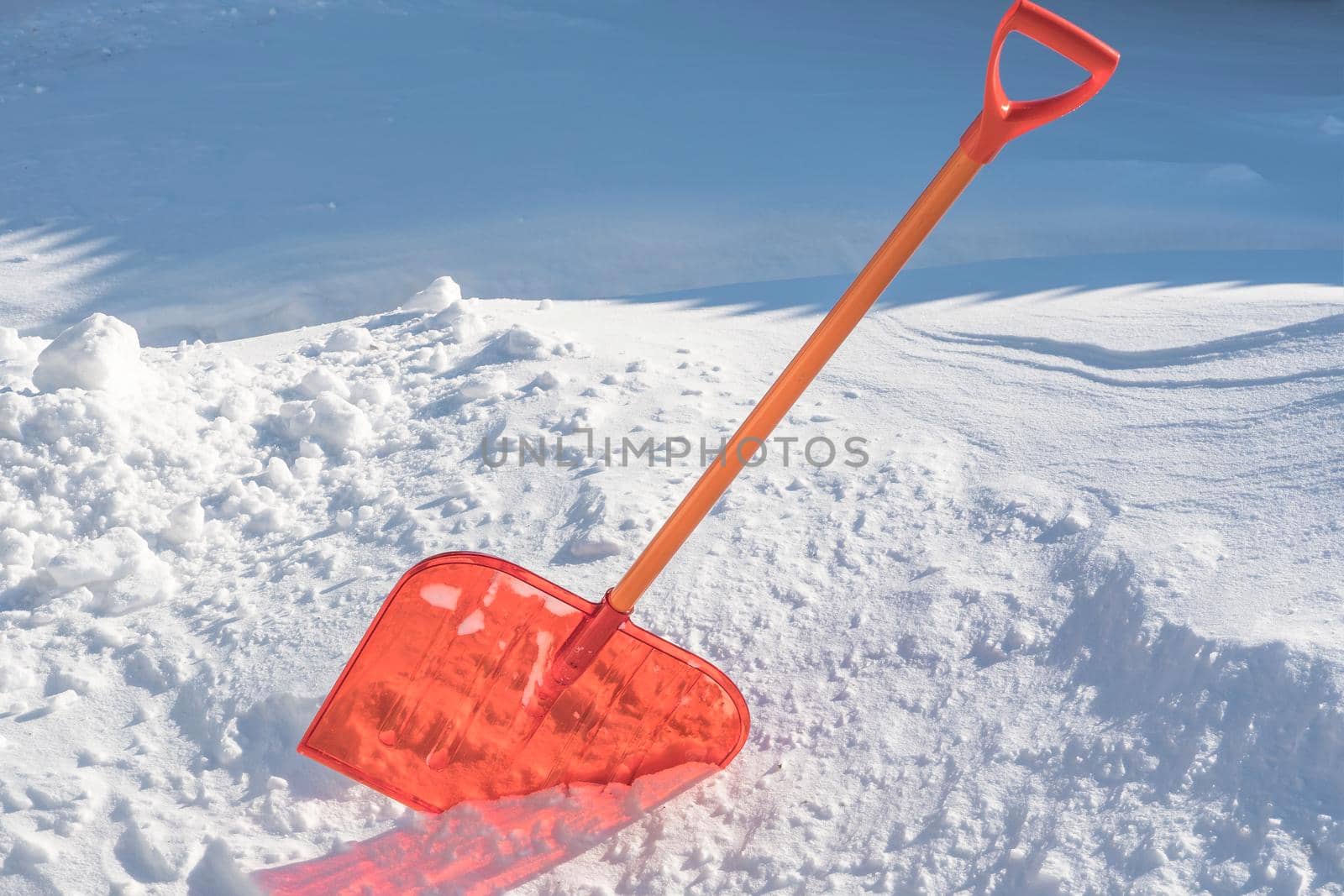 A snow shovel is stuck in a snowdrift in winter in winter. Snow removal, cleaning the street from snow drifts. A white pile of snow. Snowy weather in winter. A red shovel. Snowy Crystals