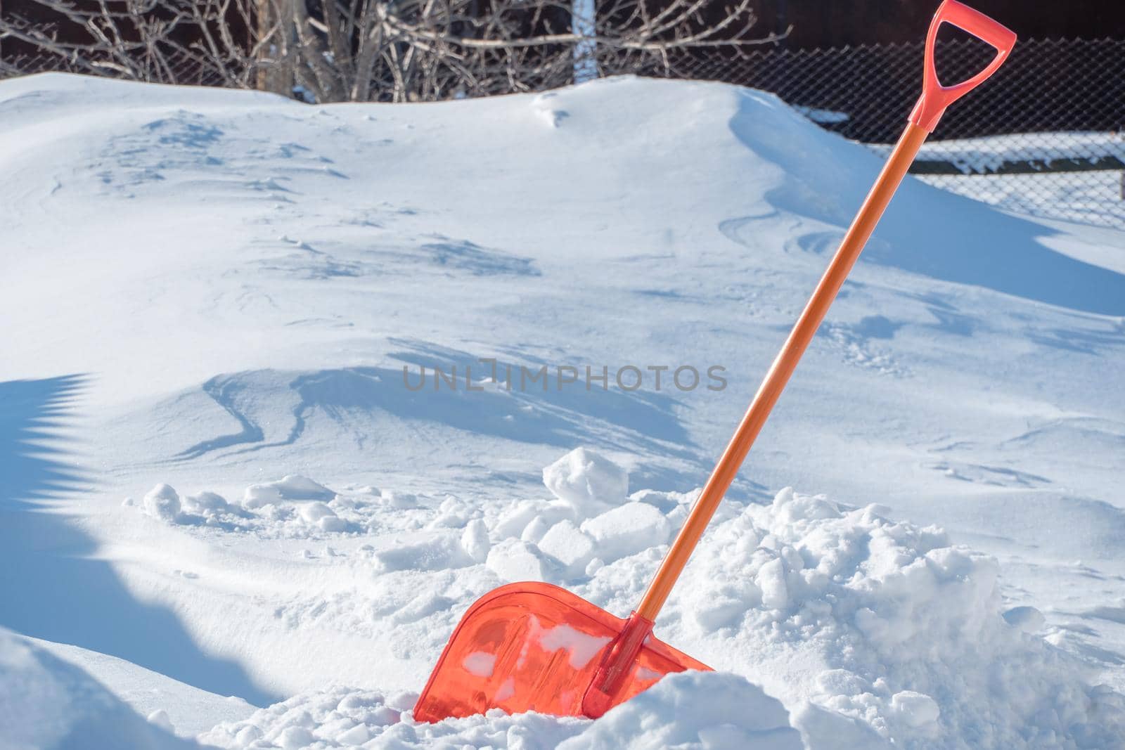 A snow shovel is stuck in a snowdrift in winter in winter. Snow removal, cleaning the street from snow drifts. A white pile of snow. Snowy weather in winter. A red shovel. Snowy Crystals