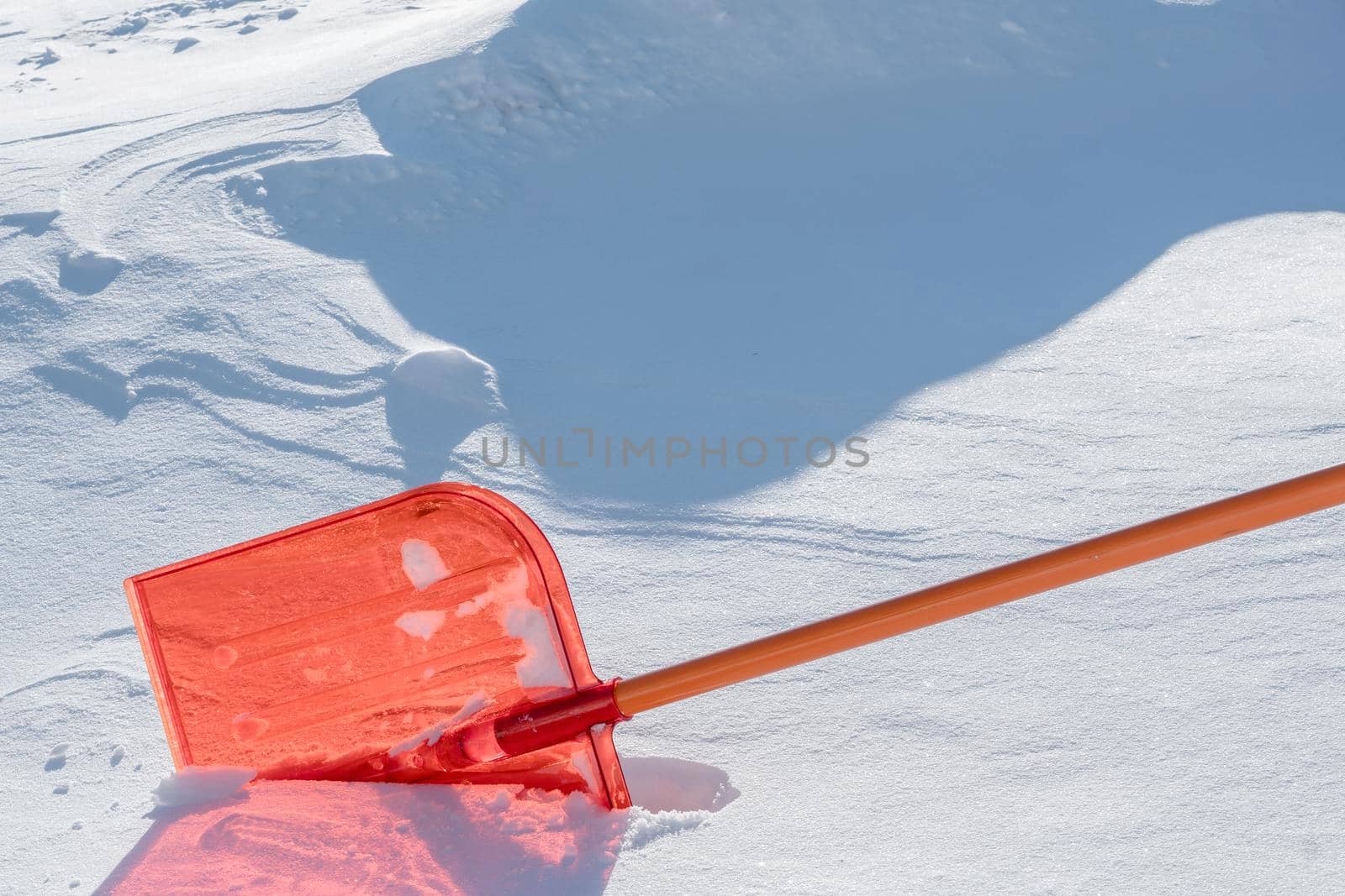 A snow shovel is stuck in a snowdrift in winter in winter. Snow removal, cleaning the street from snow drifts. A white pile of snow. Snowy weather in winter. A red shovel. Snowy Crystals by YevgeniySam