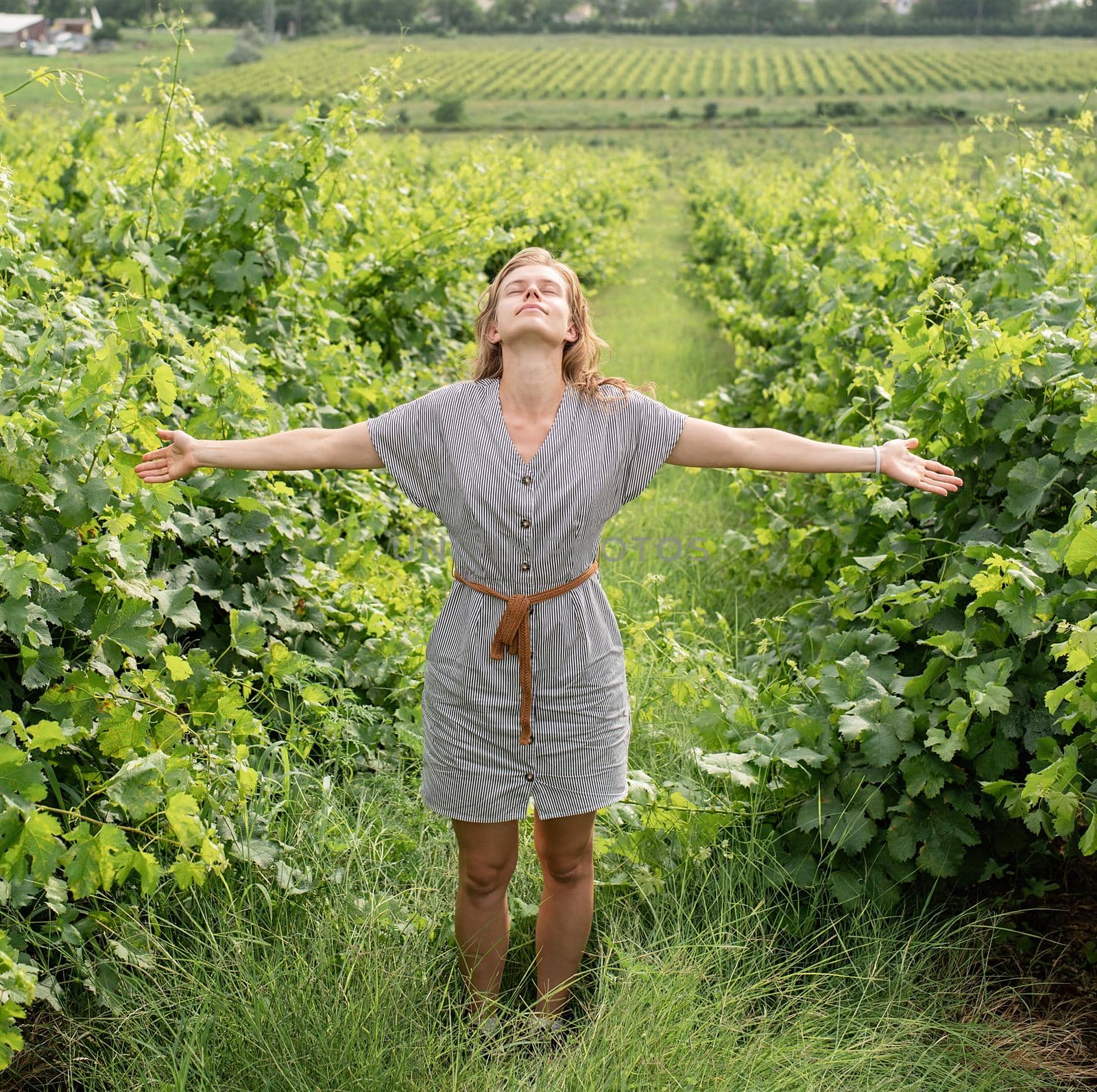 woman in summer dress walking through the vineyard smelling the grapes looking to the sky, arms outstretched