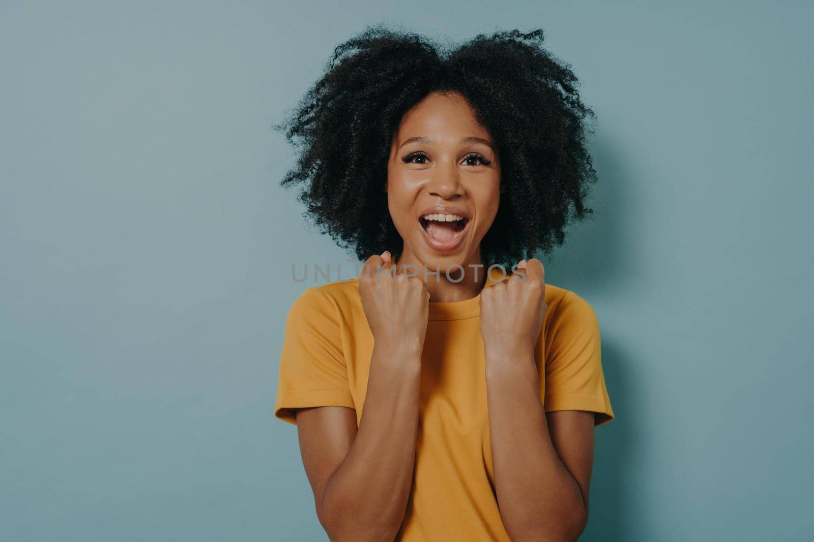 Happy dark skinned woman enjoys wonderful life, clenches fists with joy and screams. Young girl triumphs over success, feels excited. African lady rejoices goal achievement. Body language concept