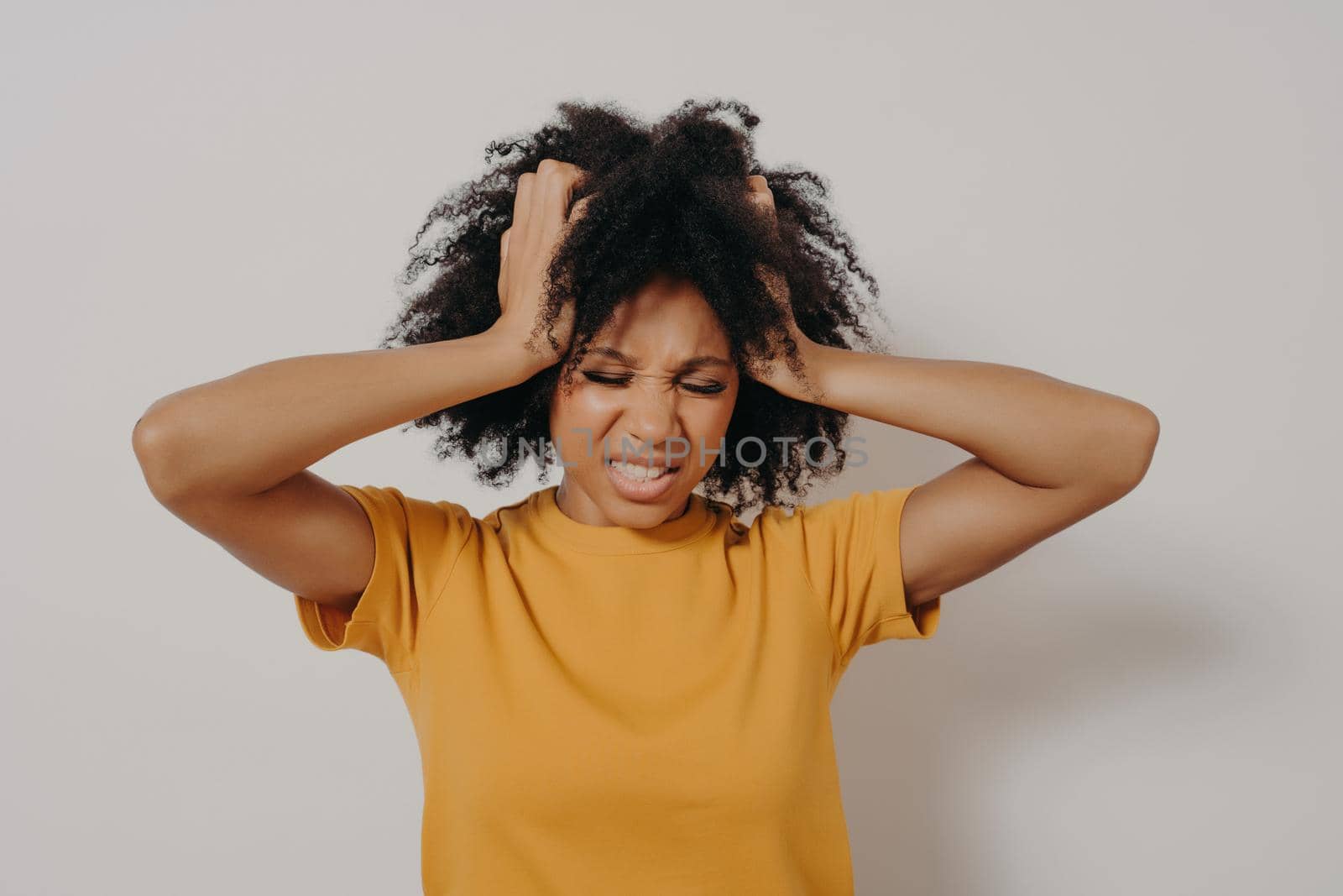 Beautiful african young woman standing in casual clothes angry and mad, screaming frustrated and furious while holding her head with hands, shouting with anger. Rage and aggressive concept