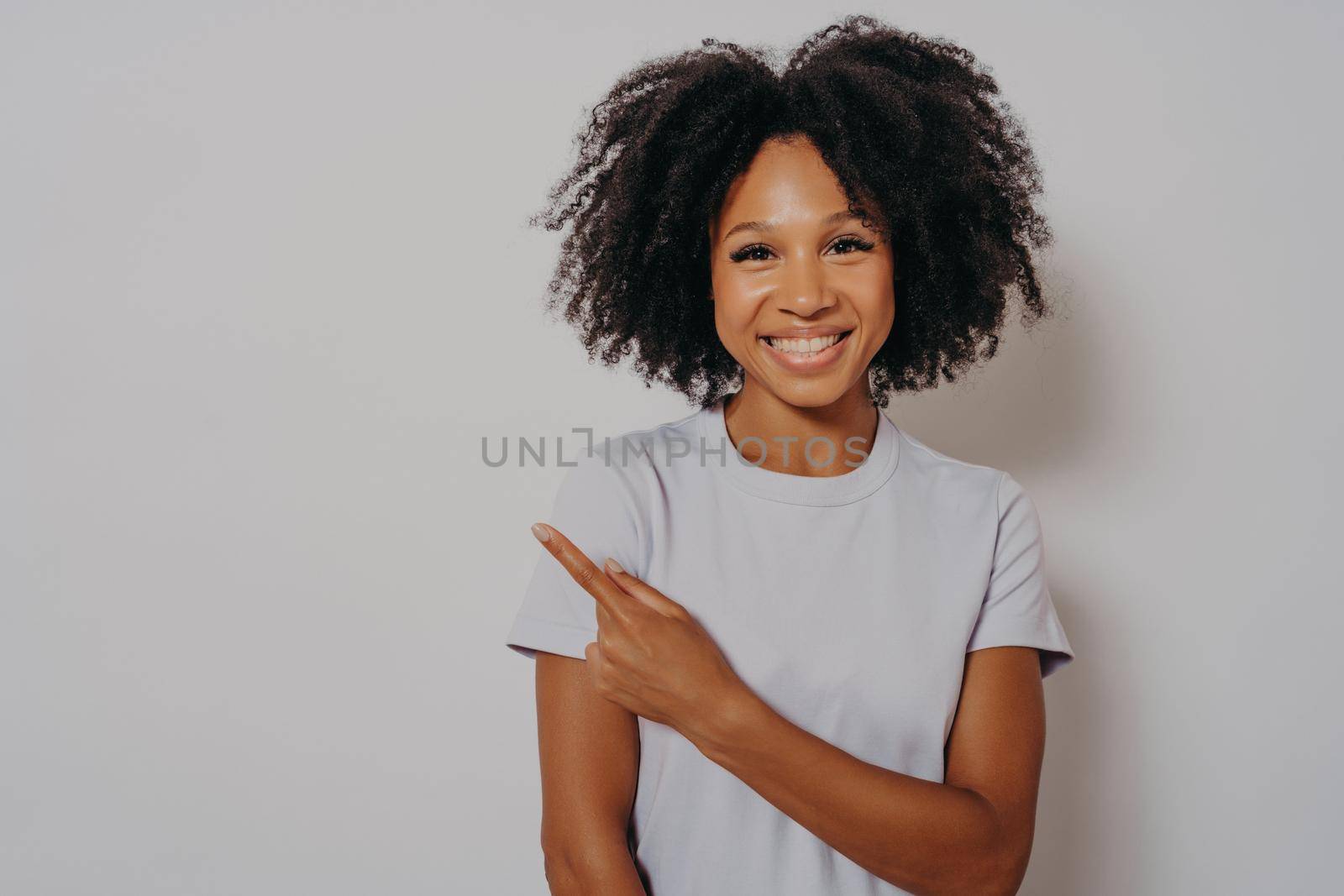 Beautiful black woman wearing casual clothes, cheerful with beaming smile on her face pointing with hand and finger up to side with happy and natural facial expression, copy space for advertising