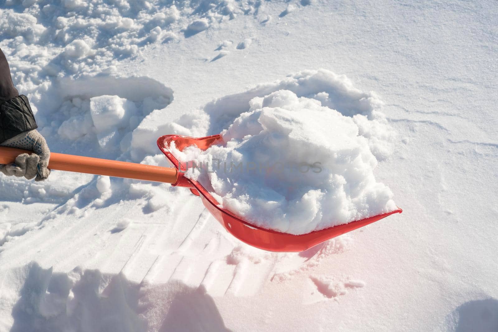 A snow shovel is stuck in a snowdrift in winter in winter. Snow removal, cleaning the street from snow drifts. A white pile of snow. Snowy frost weather in winter. A red shovel. Snowy Crystals by YevgeniySam