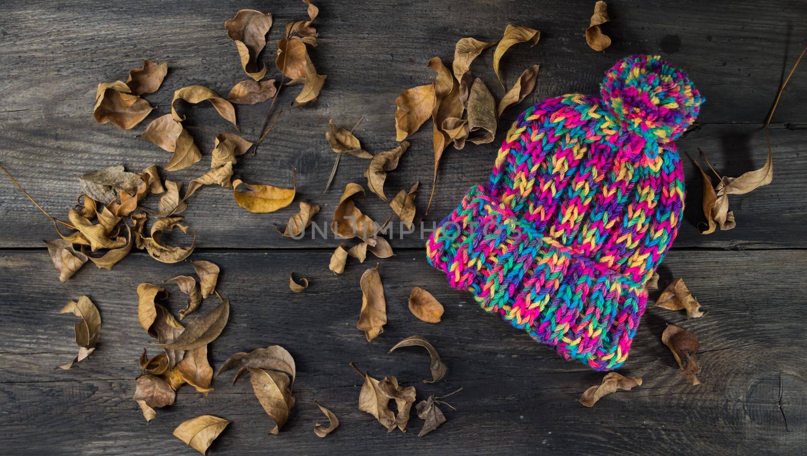hand knitted wool hats on rustic wooden background and autumn leaves by GabrielaBertolini