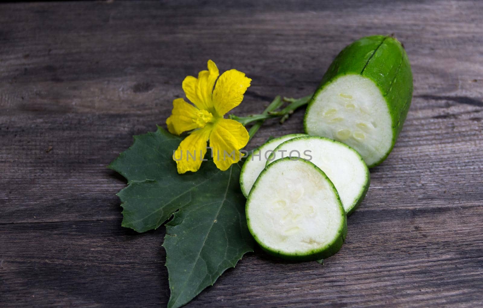 fruit and flower of the green luffa that is used for Asian cuisine, on rustic wooden background