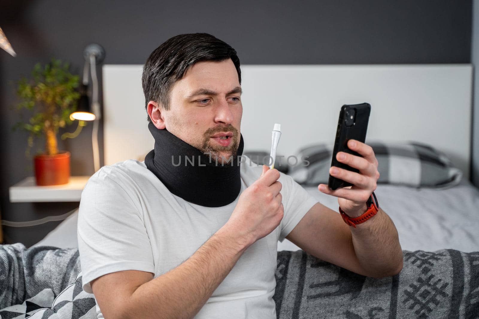 Man after accident in cervical collar consults online video call with doctor and receives recommendations for taking medications. Male in foam cervical spinal injury video conferencing with insurance by Tomashevska
