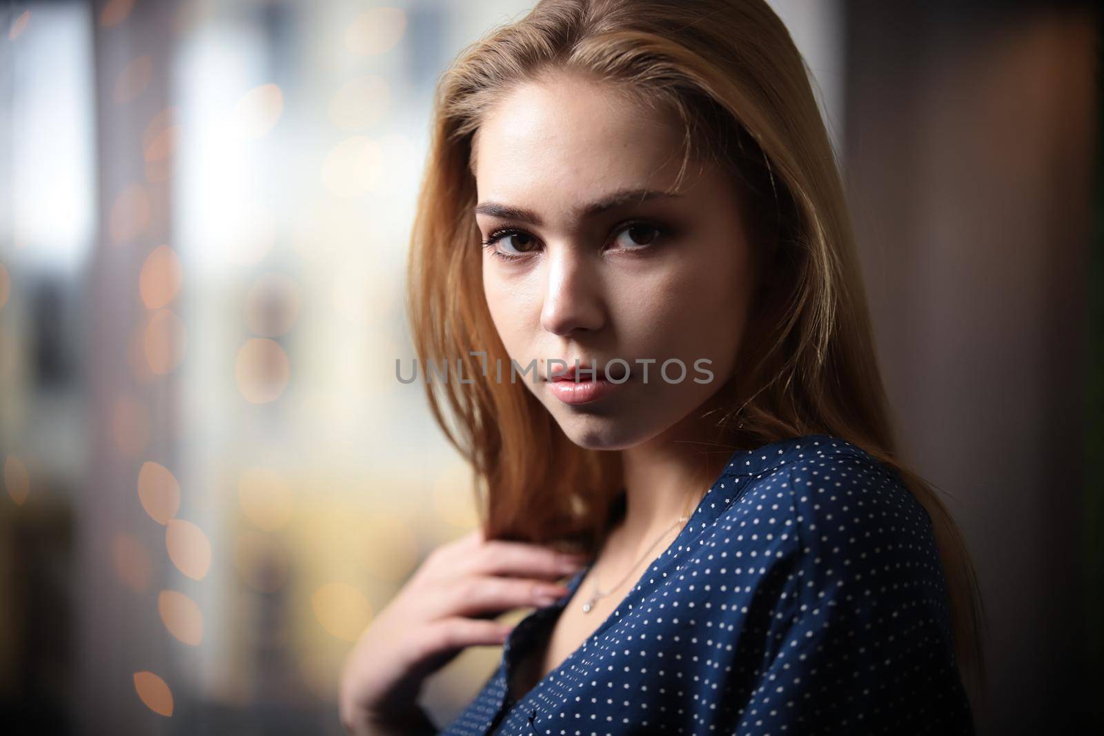 Baby face model. Portrait of beautiful young woman with blonde hair looking at camera over lights in background. Portrait