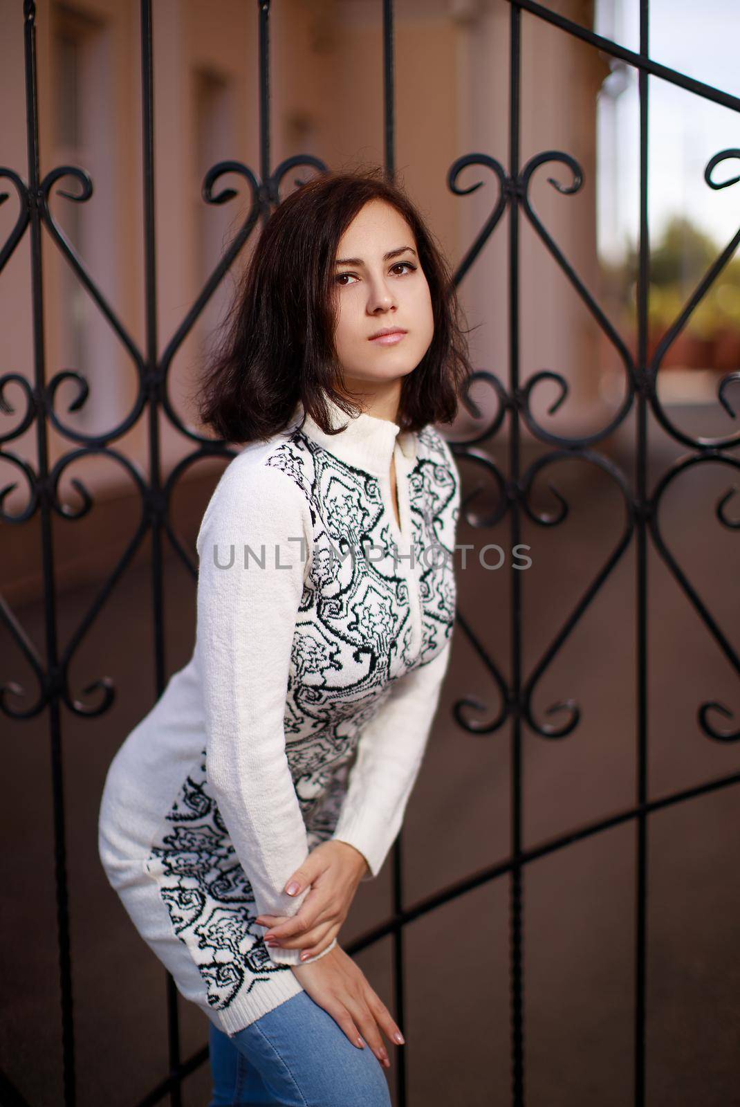 portrait of a young woman with black hair standing near the metall fence. Young woman modern portrait.