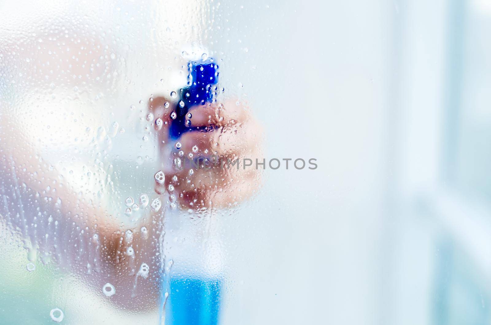 Woman hand holding bottle of blue cleaning spray, through transparent window