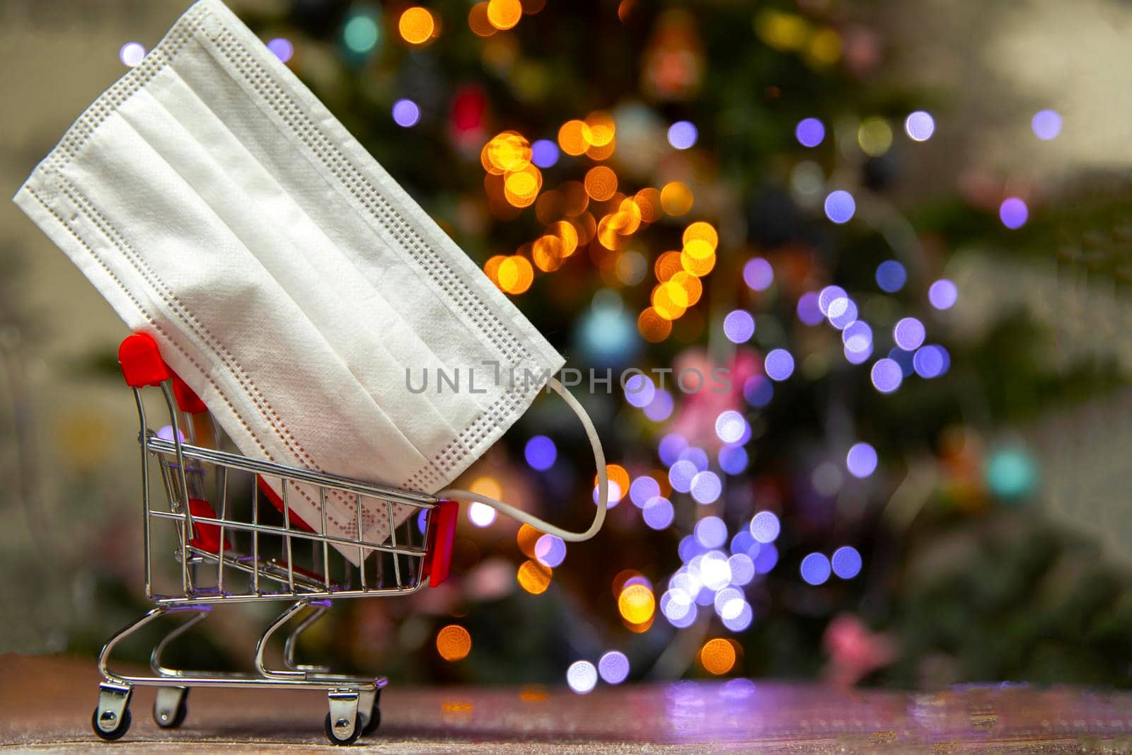 Protective safety mask in iron shopping basket near Christmas tree, Covid-19, coronavirus, holiday concept with copy space and bokeh lights background space for text