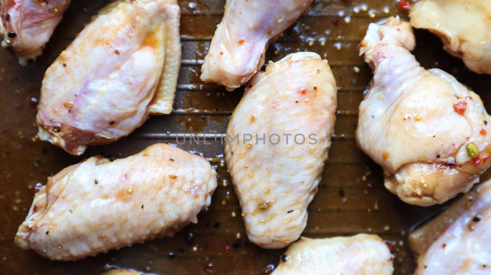 Raw pickled chicken teriyaki wings in a pan before frying. A few raw chicken wings on a baking sheet. Chicken meat in oil and in spices in a black pan, the cooking process