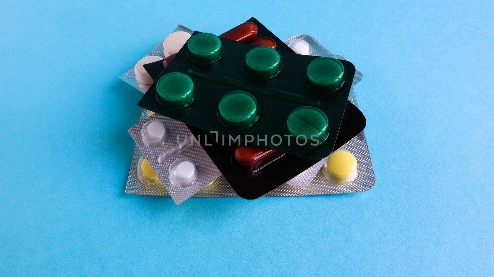 Packs of pills of various shapes and colors are stacked on a blue background. Capsules are packaged in blister packs. Different medicines. Drug treatment. Health photo. Copy space