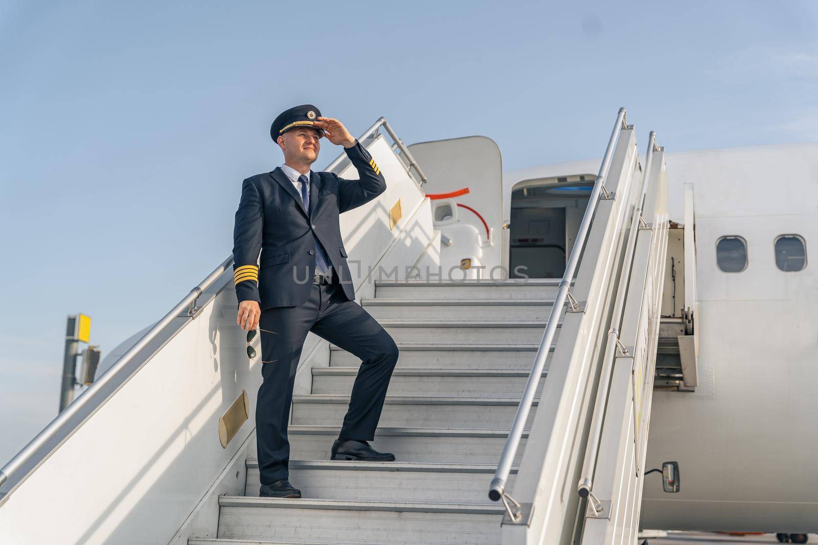 Pilot holding his hand near the cap and standing on the steps of the plane. Profession concept