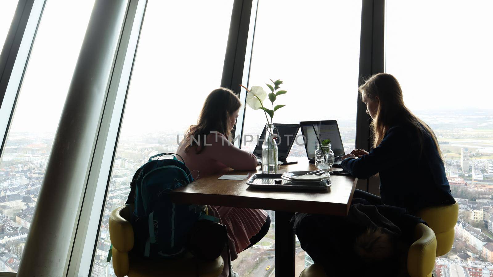 Dusseldorf, Germany - February 24, 2020: two business women are sitting with laptops by the window in the interior of a modern cafe overlooking the city. The concept of remote work, freelance