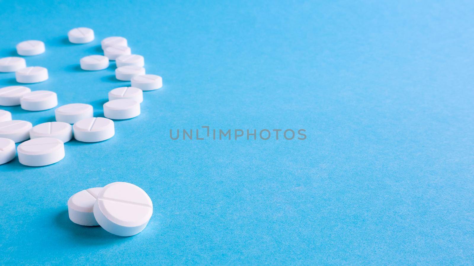 White round medical pills on a blue background. Scattered white pills on the table. The concept of medicine, pharmacy and healthcare. Copy space Empty space for text or logo