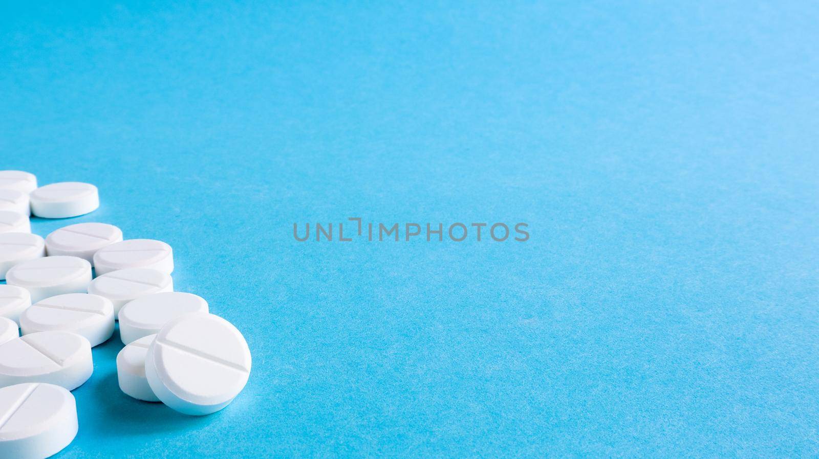 White round medical pills on a blue background. Scattered white pills on the table. The concept of medicine, pharmacy and healthcare. Copy space Empty space for text or logo