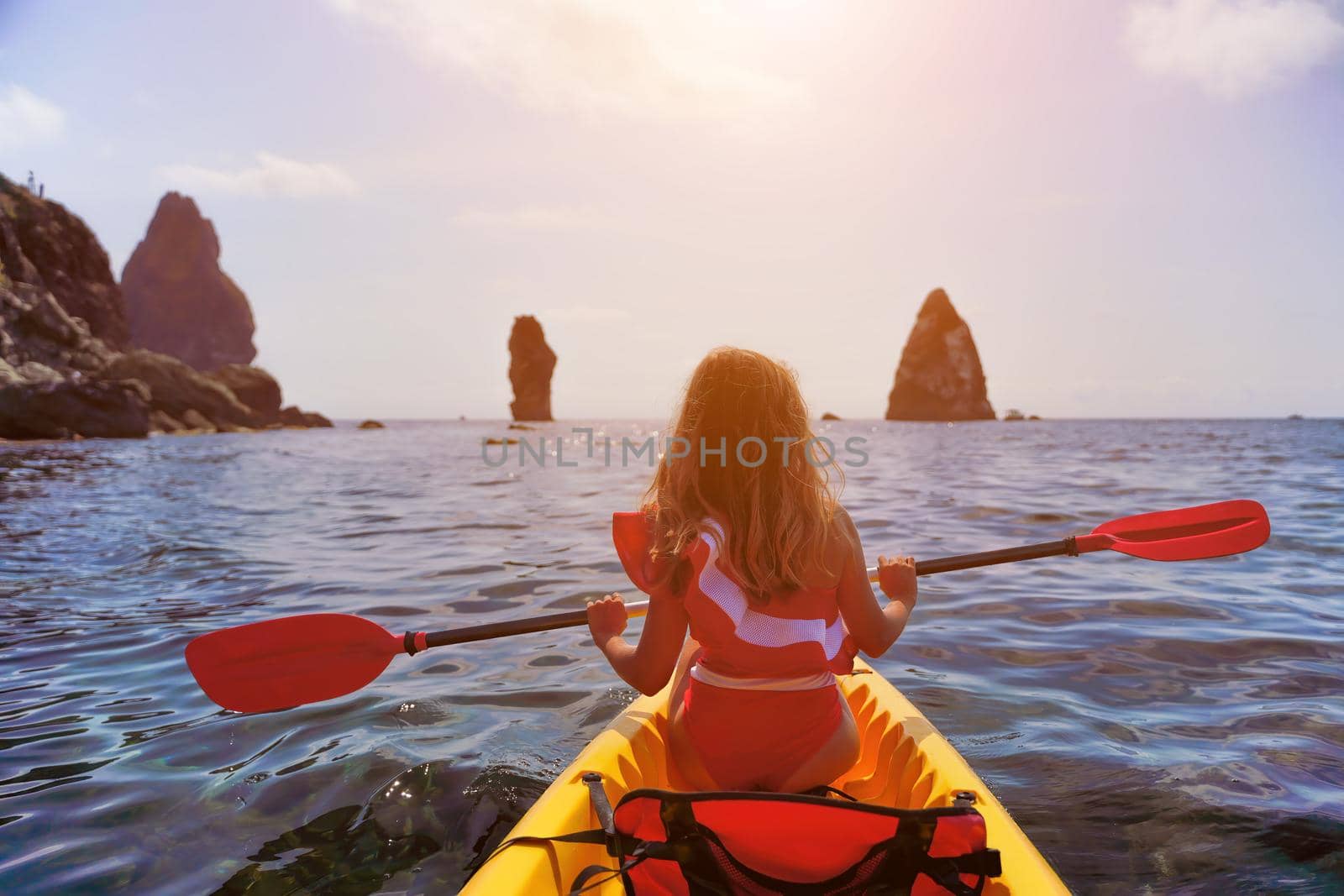 Young attractive brunette woman in red swimsuit, swimming on kayak around volcanic rocks, like in Iceland. Back view. Christmas holiday vacation and travel concept. by panophotograph