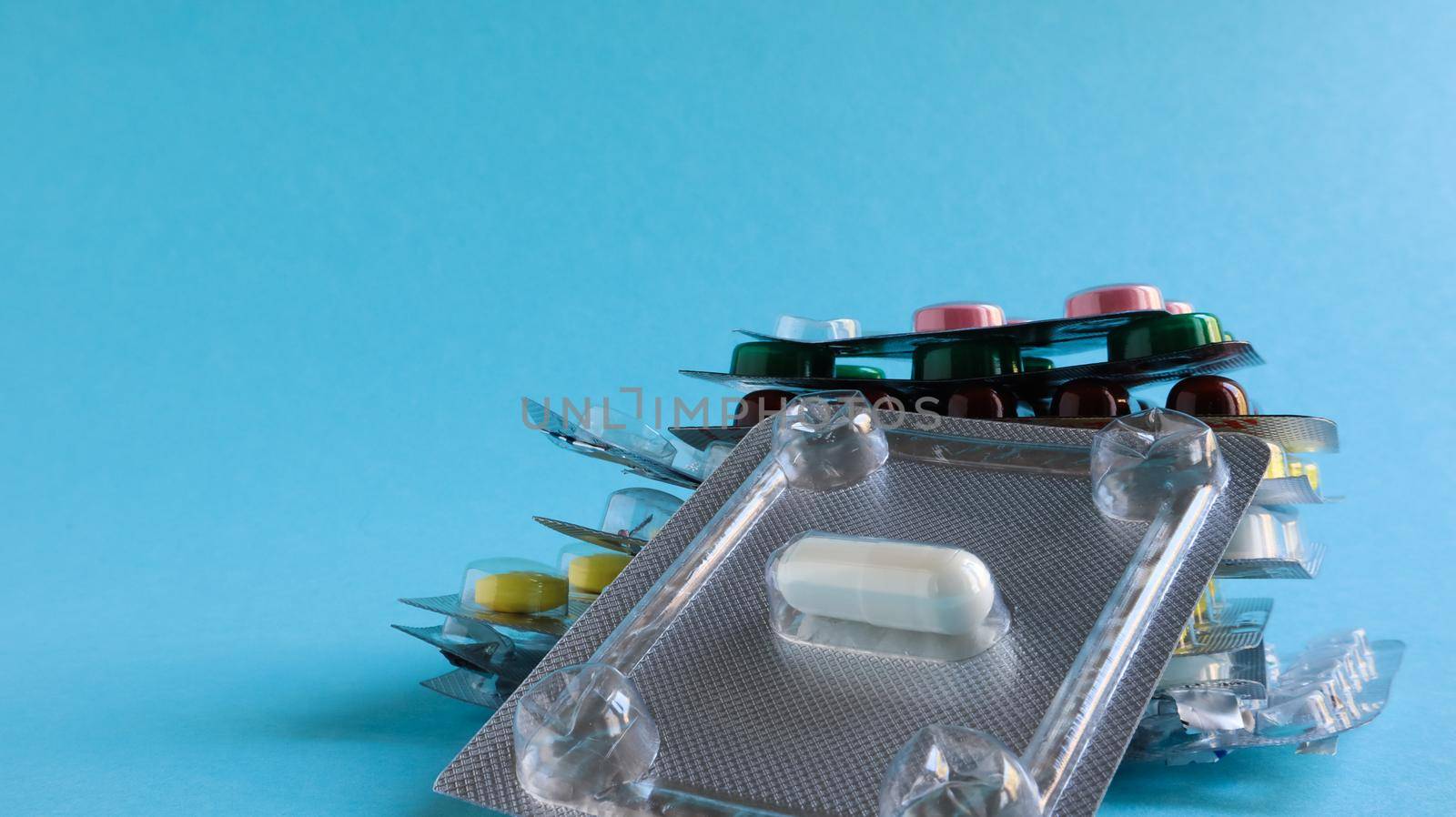 Packs of pills of various shapes and colors are stacked on a blue background. Capsules are packaged in blister packs. Different medicines. Drug treatment. Health photo. Copy space