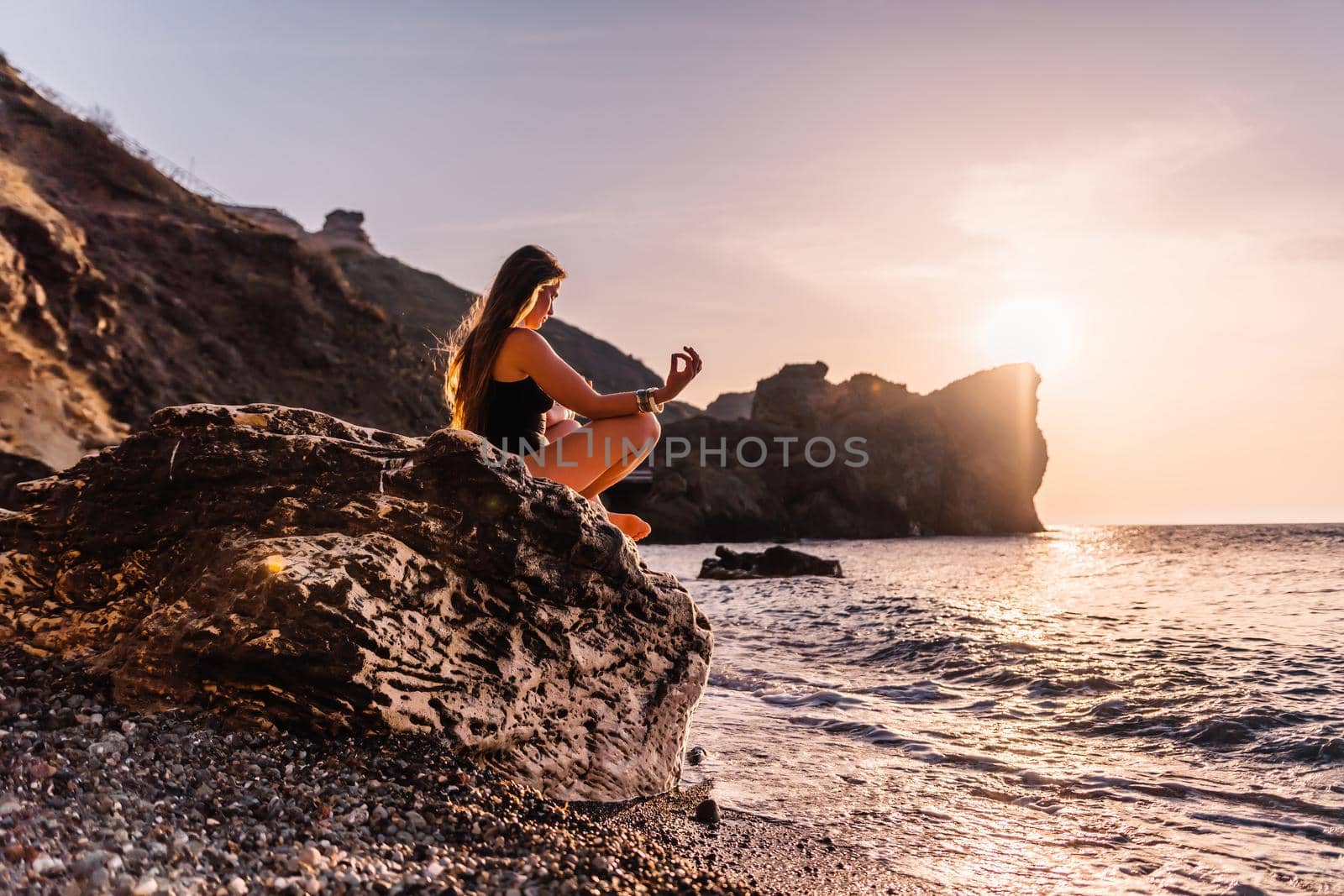 Young woman in swimsuit with long hair practicing stretching outdoors on yoga mat by the sea on a sunny day. Women's yoga fitness pilates routine. Healthy lifestyle, harmony and meditation concept.