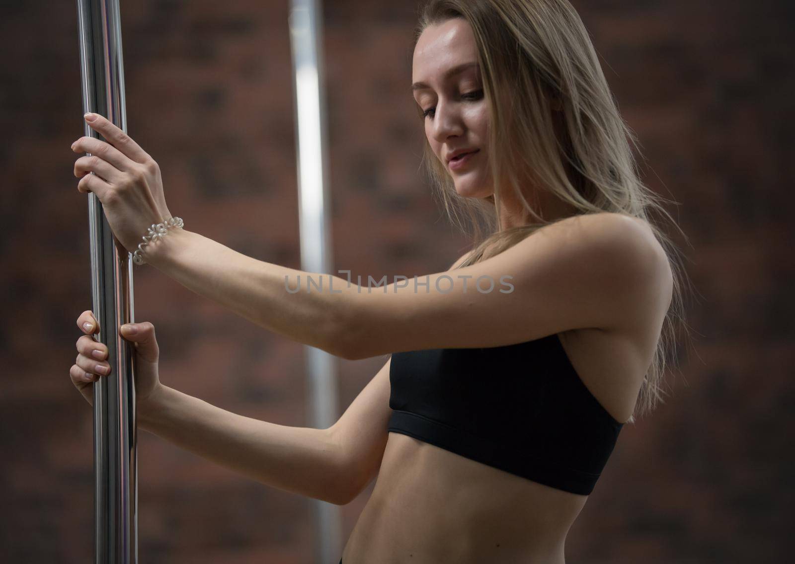 Young attractive woman in sport bra staying holding a pole. Portrait