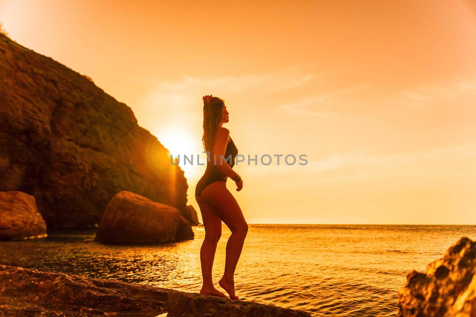 Young woman with long hair in black swimsuit and boho style braclets practicing outdoors on yoga mat by the sea on a sunset. Women's yoga fitness routine. Healthy lifestyle, harmony and meditation by panophotograph