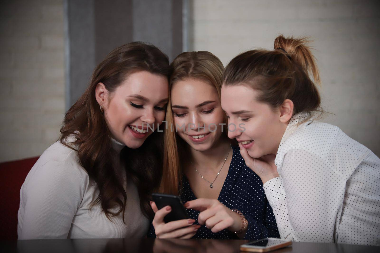 Three young beautiful women sitting in a bar looking on a phonescreen. Portrait