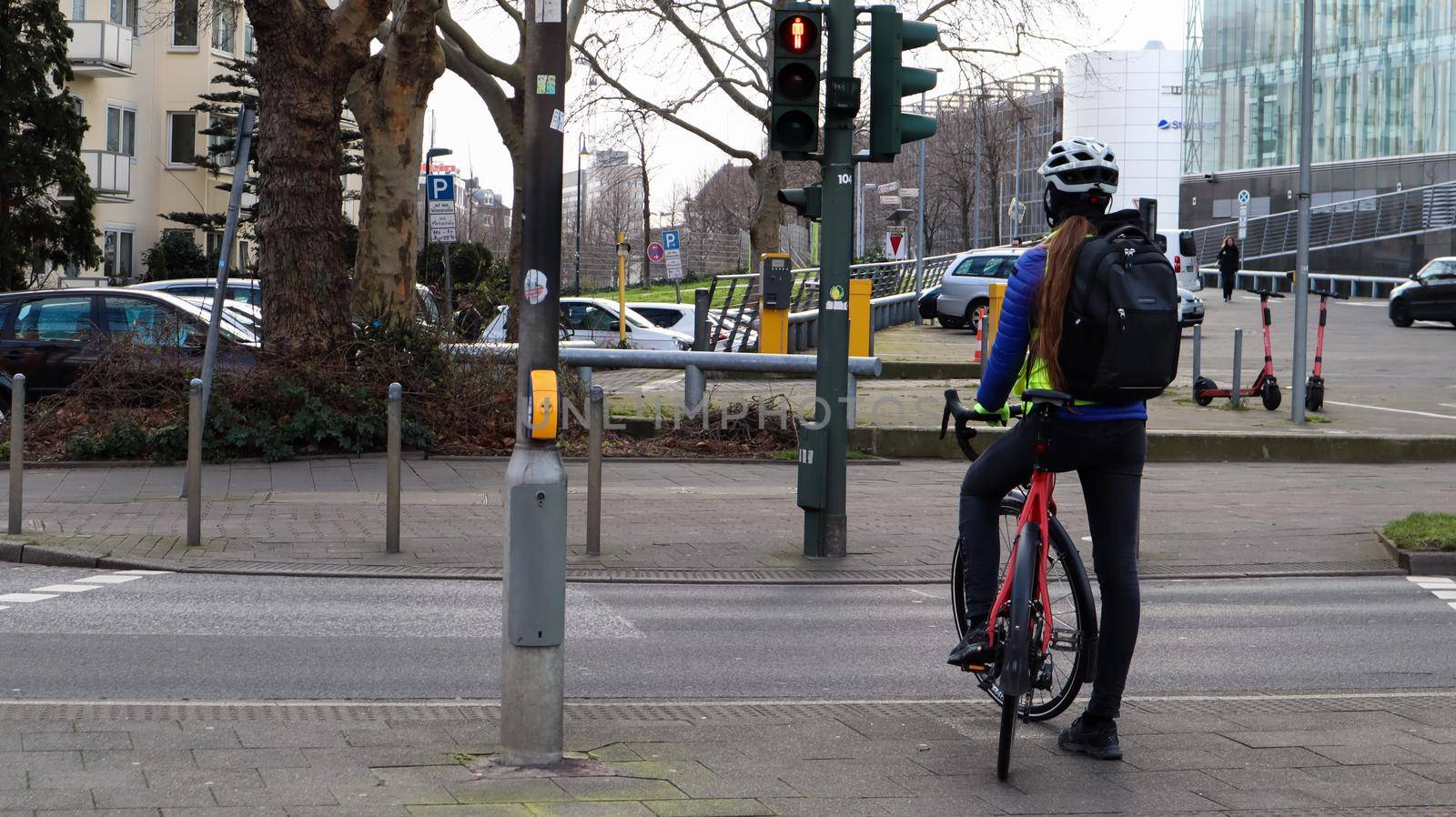 Germany, Dusseldorf - February 28, 2020: A young girl a cyclist in a helmet, stopped at a traffic light and waiting for a permission signal to cross the street. City view