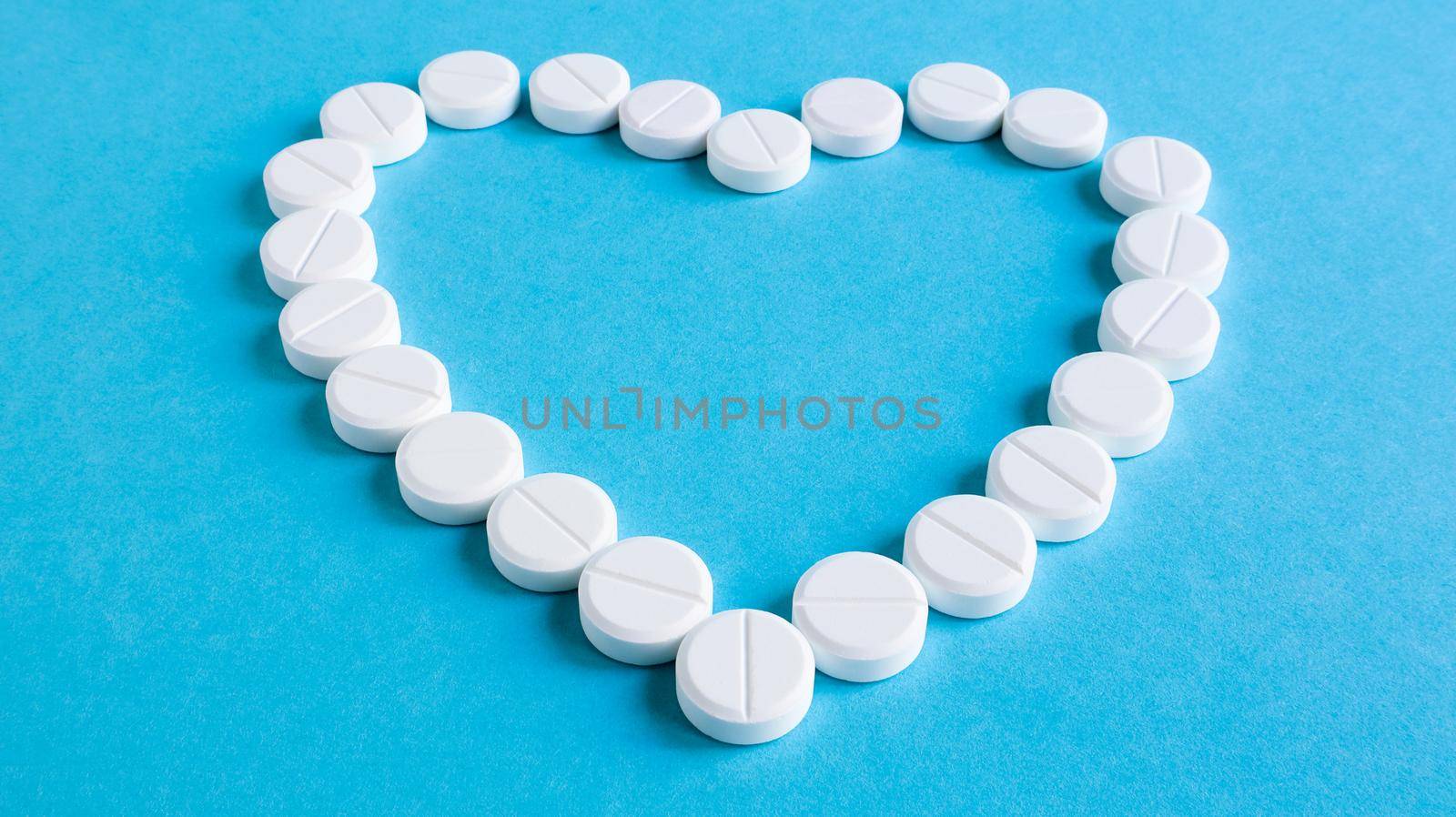 White round pills laid out in the shape of a heart on a blue background. Health symbol made of pills for therapy, treatment and healthcare concept. A medicine for lovers or potency, heart disease