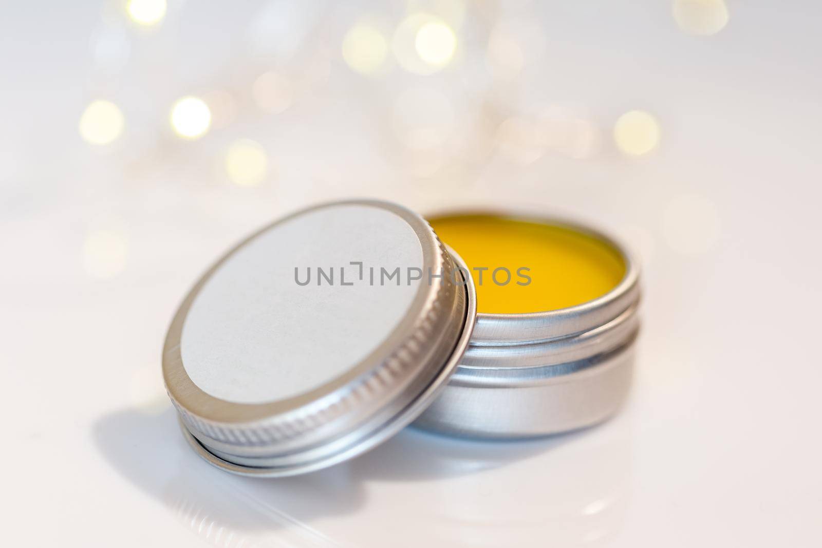 Lip balm in metal jar over sparkling light bokeh background. Empty label mock up. Natural cosmetic winter care product. Selective focus