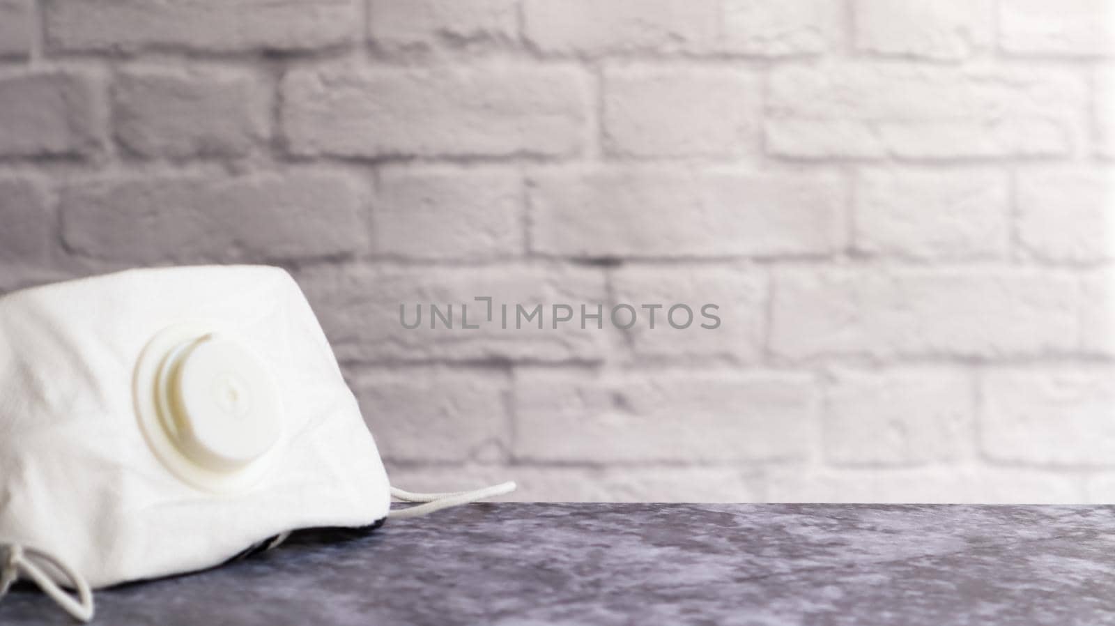White face shield with flap on a gray table against a white brick wall with copy space. medical masks during outbreaks of viral diseases such as coronavirus or COVID-19 pandemic