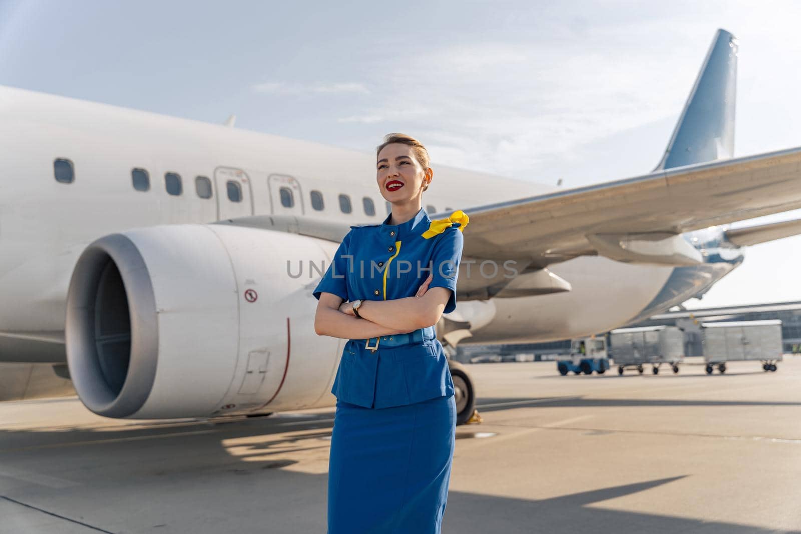Happy female flight attendant posing near big plane by Yaroslav_astakhov